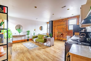 A modern kitchen with a stove, a dining area with a table and chairs, a green sofa, and a brick wall. - Jungle House Luxury Lofts – Short North High Street (Columbus)