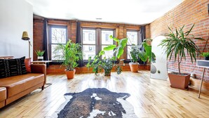 A room with a brown leather sofa, a black and white rug, and multiple potted plants. - Jungle House Luxury Lofts – Short North High Street (Columbus)