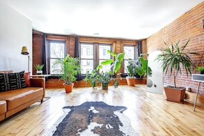A room with a brown leather sofa, a black and white rug, and multiple potted plants. - Jungle House Luxury Lofts – Short North High Street (Columbus)