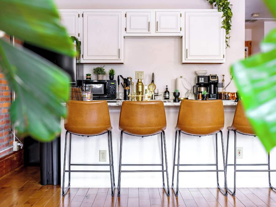 A kitchen with white cabinets, a brick wall, and a bar area with stools.
