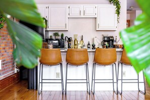 A kitchen with white cabinets, a brick wall, and a bar area with stools. - Jungle House Luxury Lofts – Short North High Street (Columbus)