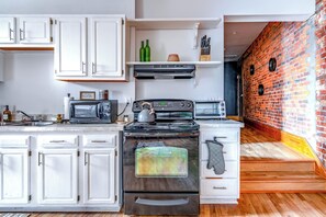 A kitchen with white cabinets, a stove, a microwave, and a brick wall. - Jungle House Luxury Lofts – Short North High Street (Columbus)