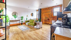 A modern kitchen with a stove, a dining area with a table and chairs, a green sofa, and a brick wall. - Jungle House Luxury Lofts – Short North High Street (Columbus)