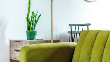 Un sofá verde, una lámpara de pie, una planta en maceta, un espejo y una silla en una habitación con piso de madera.