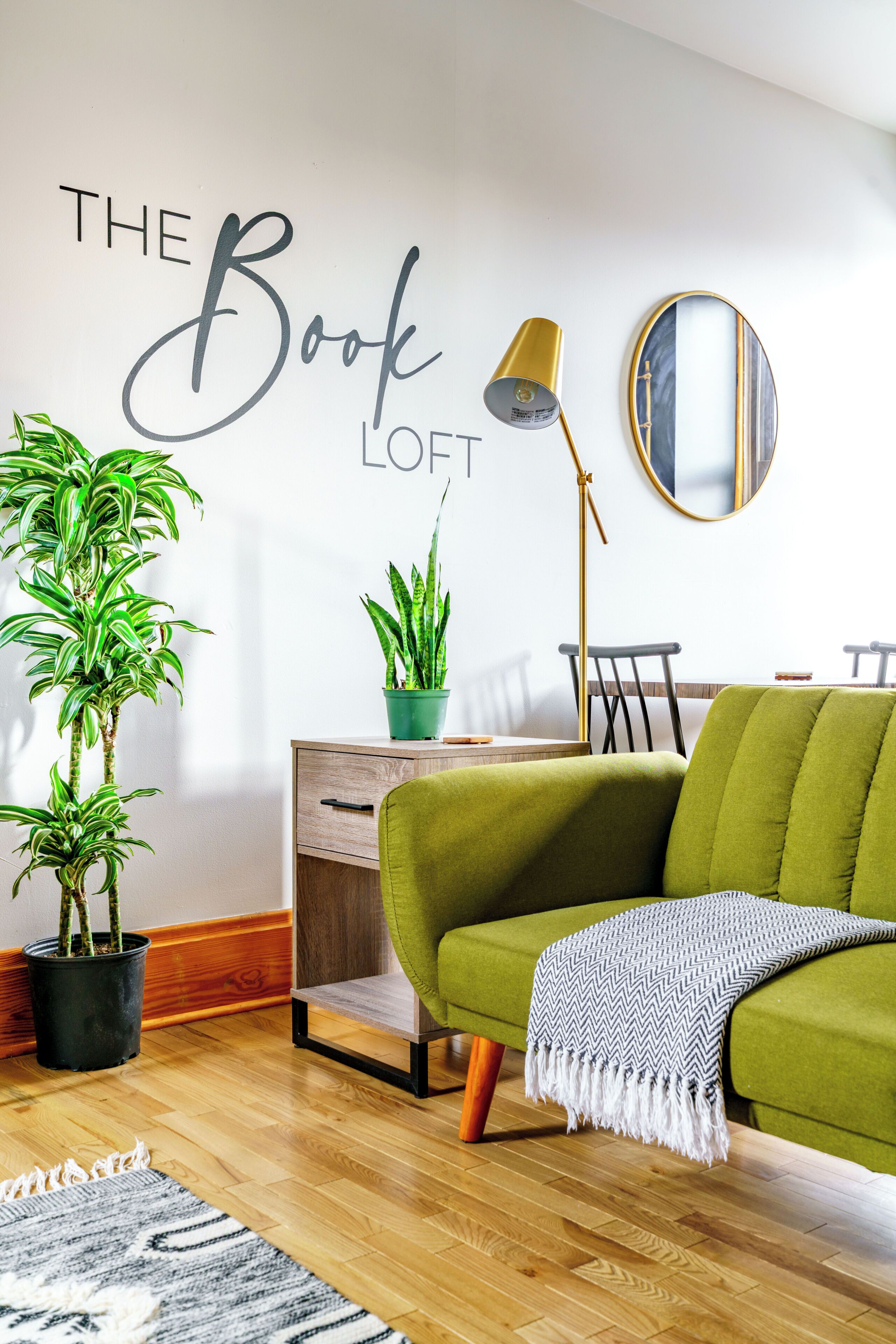 A modern living room with a green sofa, a small table, a lamp, and two potted plants.