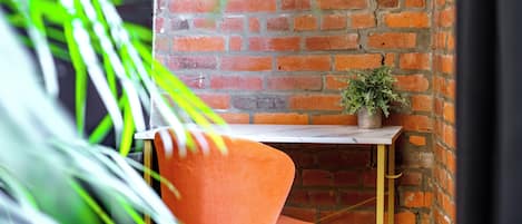 Un rincón con pared de ladrillo, una mesa, una silla y una planta en maceta.
