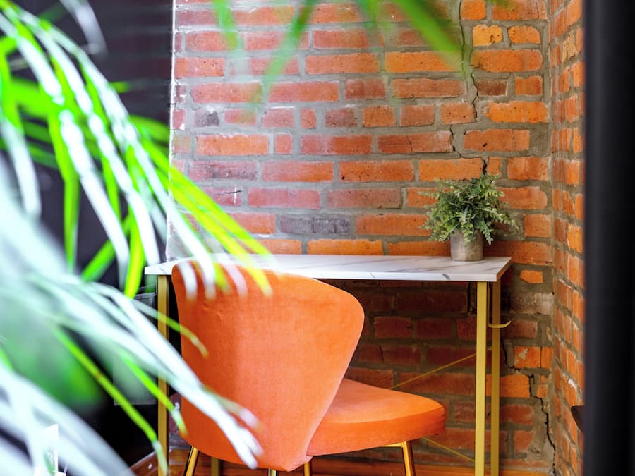 A corner with a brick wall, a table, a chair, and a potted plant.