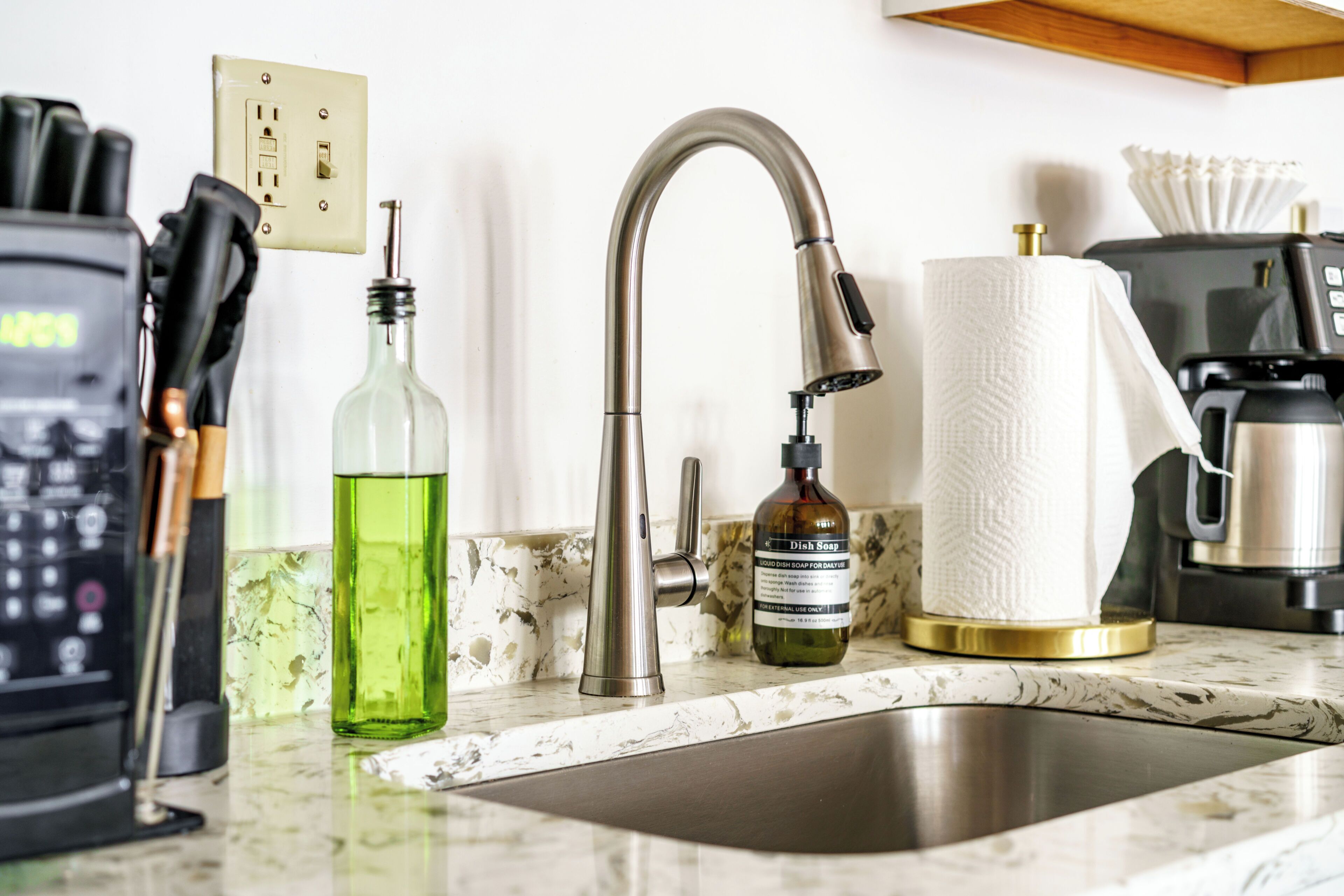 A kitchen sink with a modern faucet, a bottle of dish soap, a paper towel holder, and a coffee maker on the countertop.