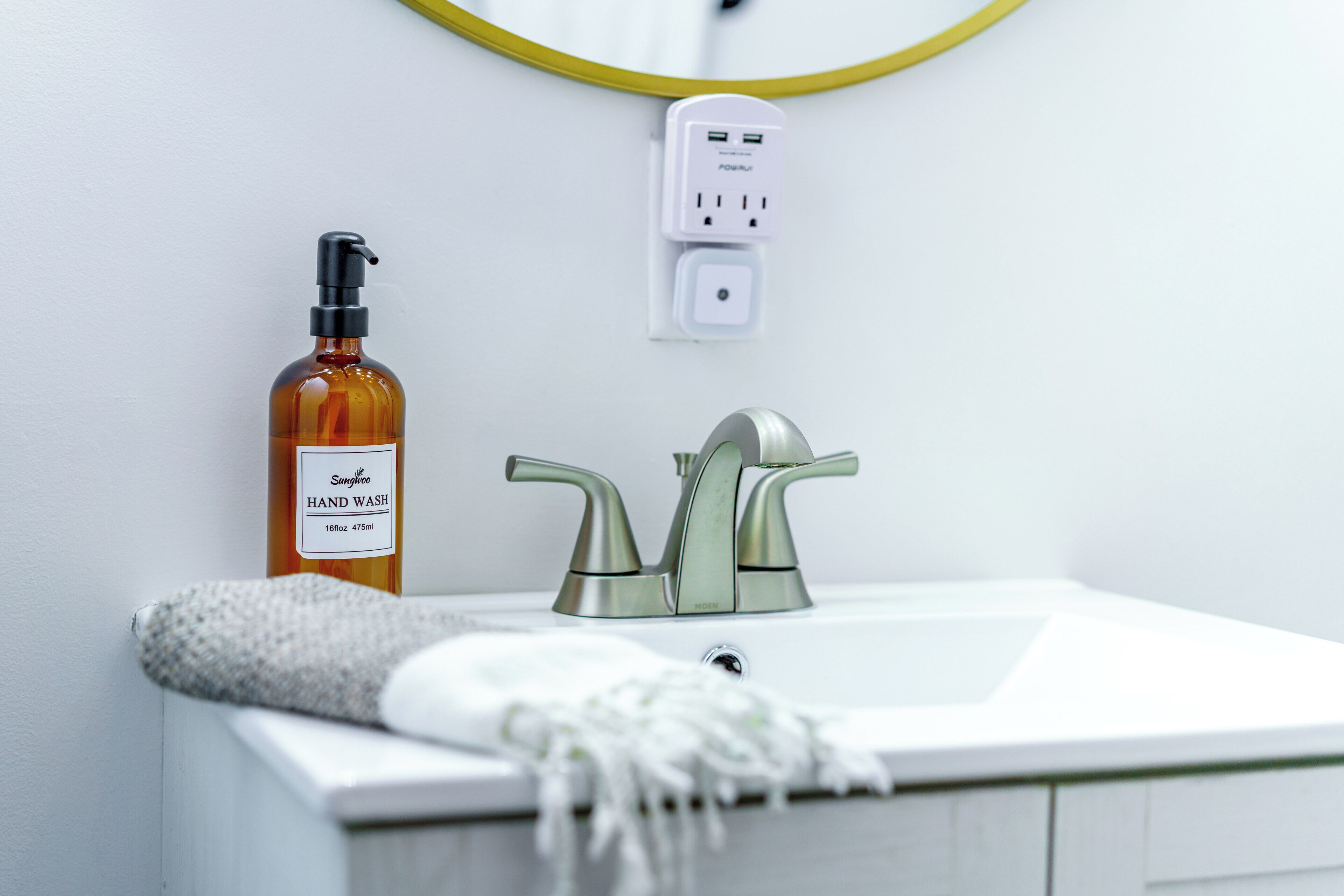Un baño con un lavabo blanco, una botella dispensadora de jabón, un grifo y un enchufe.