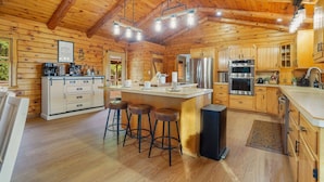 A wooden cabin interior with a kitchen featuring a central island, bar stools, and modern appliances. - Luxury Retreat in the heart of Perry County, PA. There are plenty of amenities for the whole family to enjoy! (Elliottsburg)