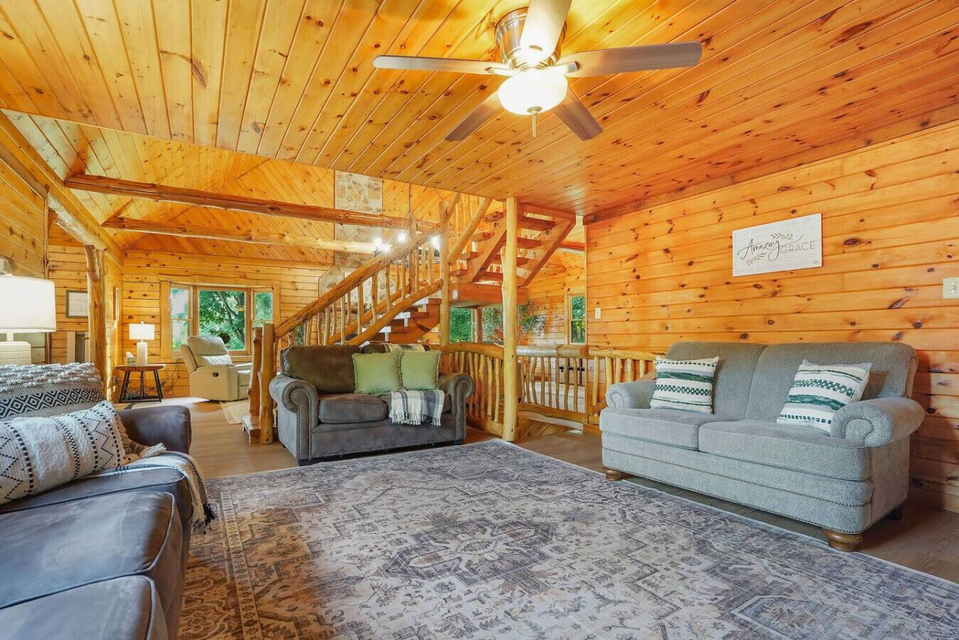 A wooden interior with a staircase, two sofas, a rug, and a ceiling fan.