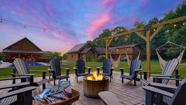 An outdoor deck with Adirondack chairs, a fire pit, and a wooden pergola with string lights. - Luxury Retreat in the heart of Perry County, PA. There are plenty of amenities for the whole family to enjoy! (Elliottsburg)