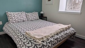 A bedroom with a bed, a nightstand, a window, and a wall-mounted picture. - The Loft at Spruce Lane (Ingonish)