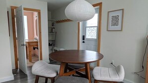 A dining area with a round table and four chairs, a hanging light fixture, and a wooden floor. - The Loft at Spruce Lane (Ingonish)