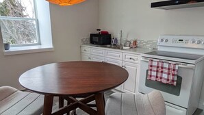 A modern kitchen with white cabinets, a stove, and a hanging orange light fixture. - The Loft at Spruce Lane (Ingonish)