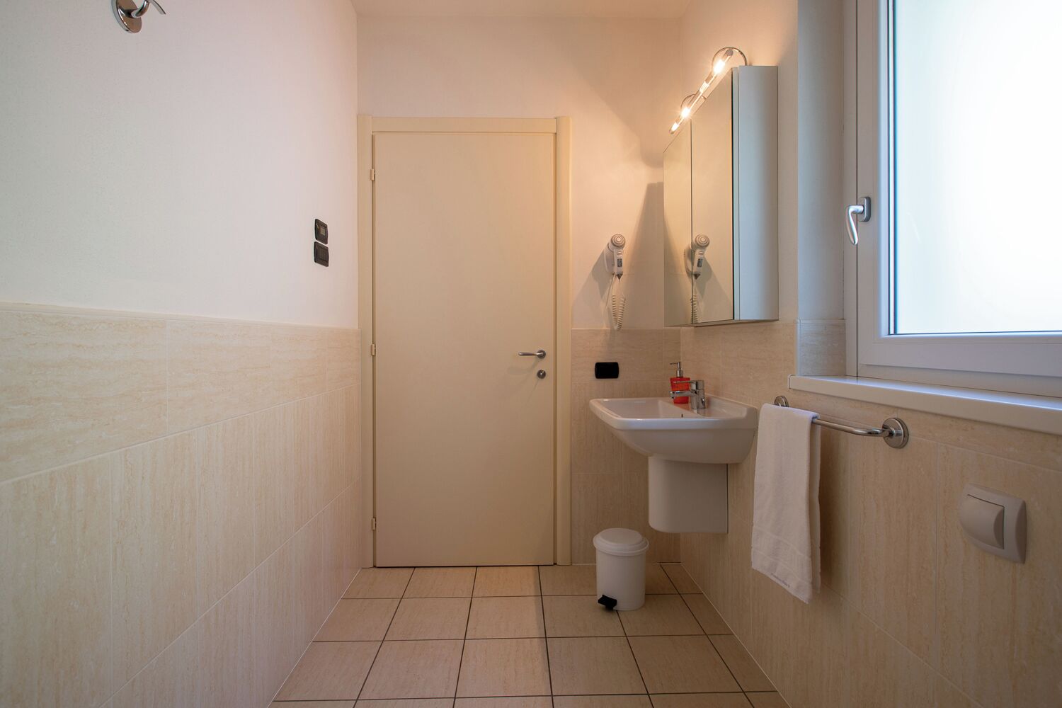 Une petite salle de bain avec une porte blanche, un lavabo avec un miroir et une fenêtre.