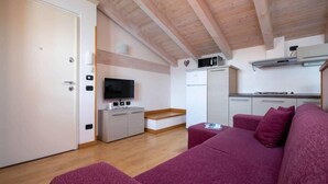 Un espace de vie compact doté d’un plafond en bois, d’un coin cuisine, d’une télévision et d’un canapé rouge.