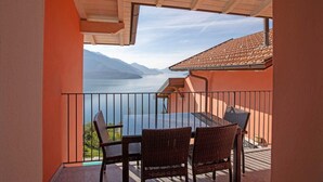 Un balcon avec des fauteuils en osier et une table, donnant sur un lac avec des montagnes en arrière-plan.