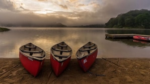 Three red boats lined up on a sandy shore by a calm lake with a cloudy sky.