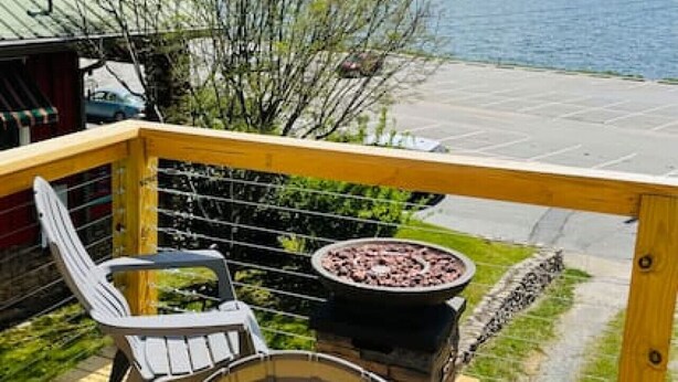A wooden deck with two chairs and a grill, overlooking a lake with trees and mountains in the background.