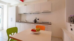 A modern kitchen with white cabinets, a gas stove, and a bowl of fruit on the table.