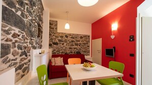 A compact living space with a stone wall, a red accent wall, a white table with a fruit bowl, and colorful chairs.