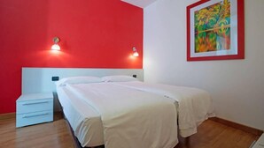 A bedroom with a bed, a nightstand, a red wall, and a framed painting.