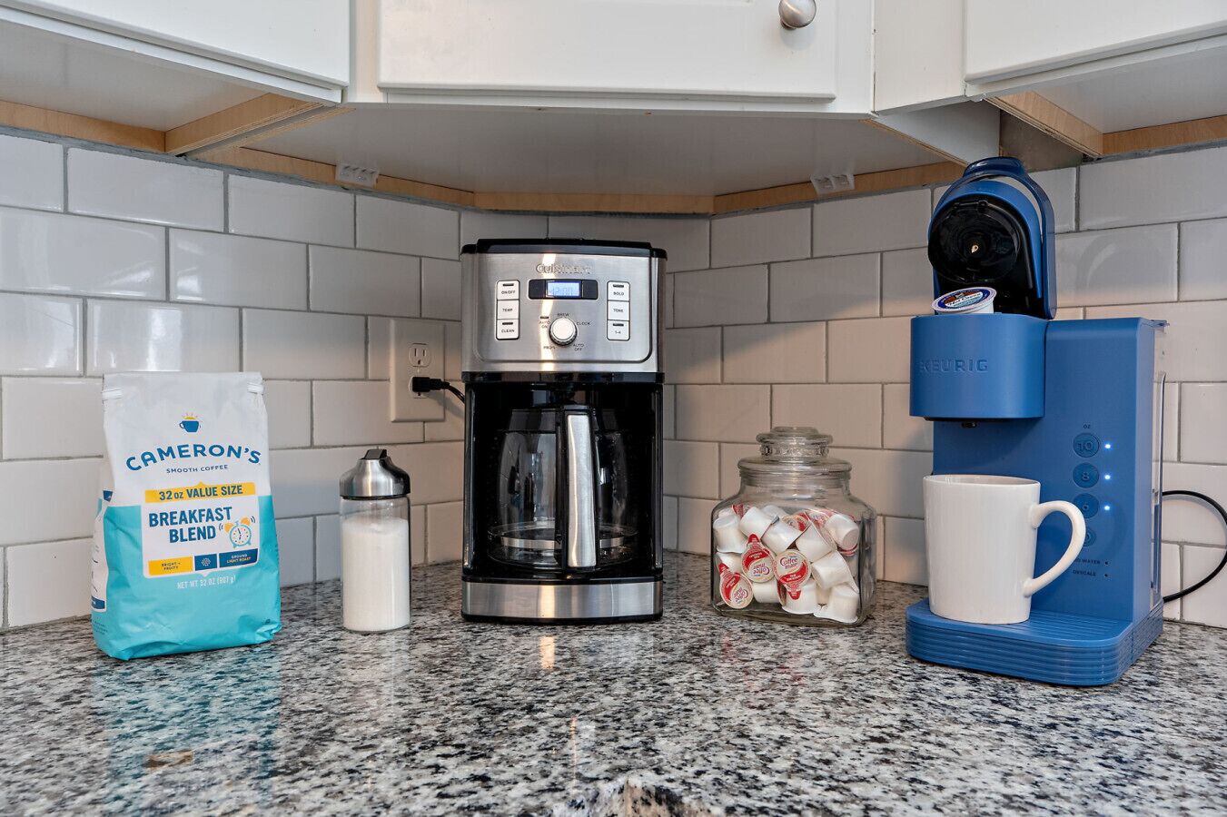 A kitchen with a coffee maker, a bag of coffee, a milk jug, and a coffee machine.
