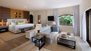 Una habitación de hotel moderna con cama, sofá y mesa de centro, televisor y ventana con cortinas.