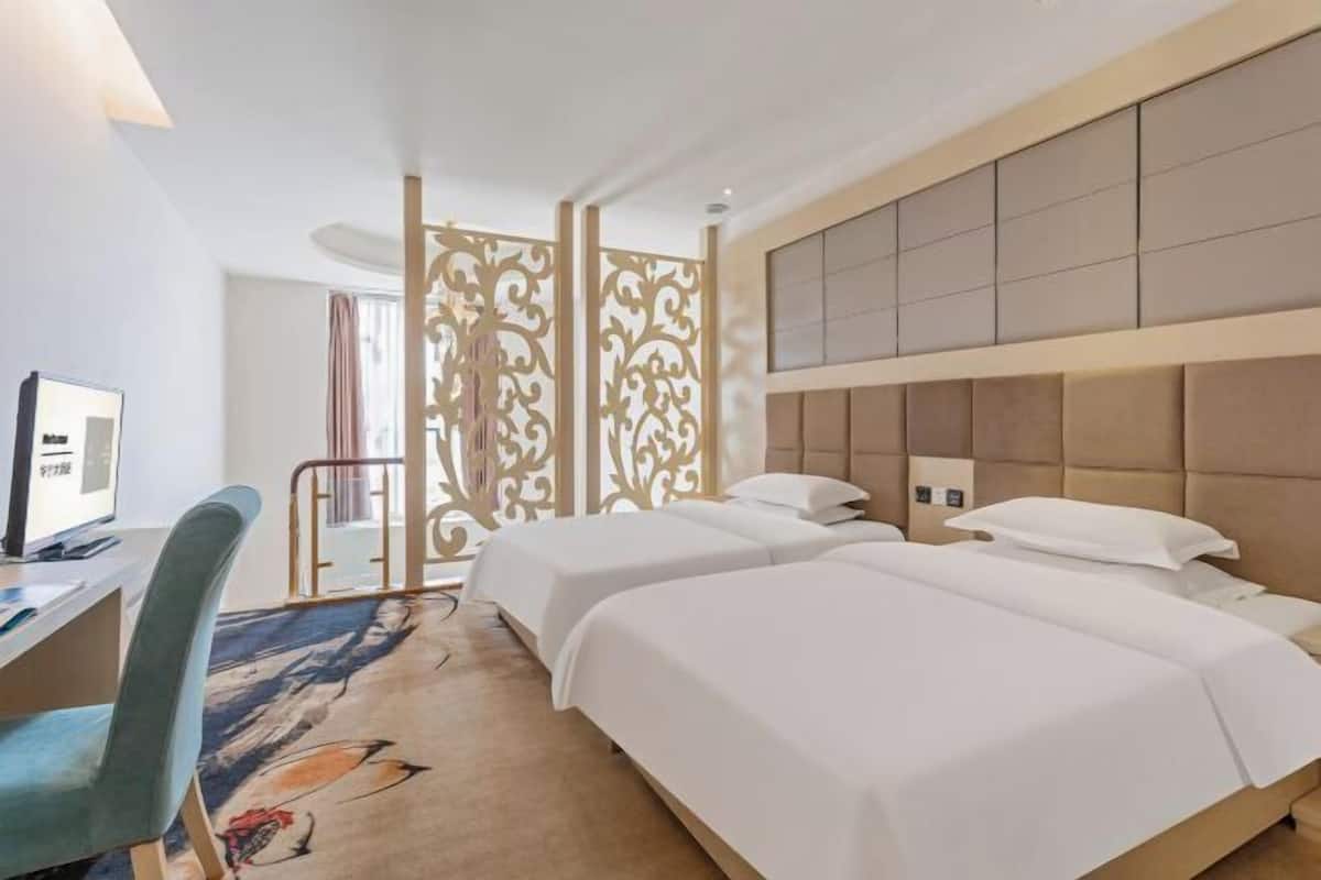 A hotel room with two beds, a desk with a computer, and a decorative partition.