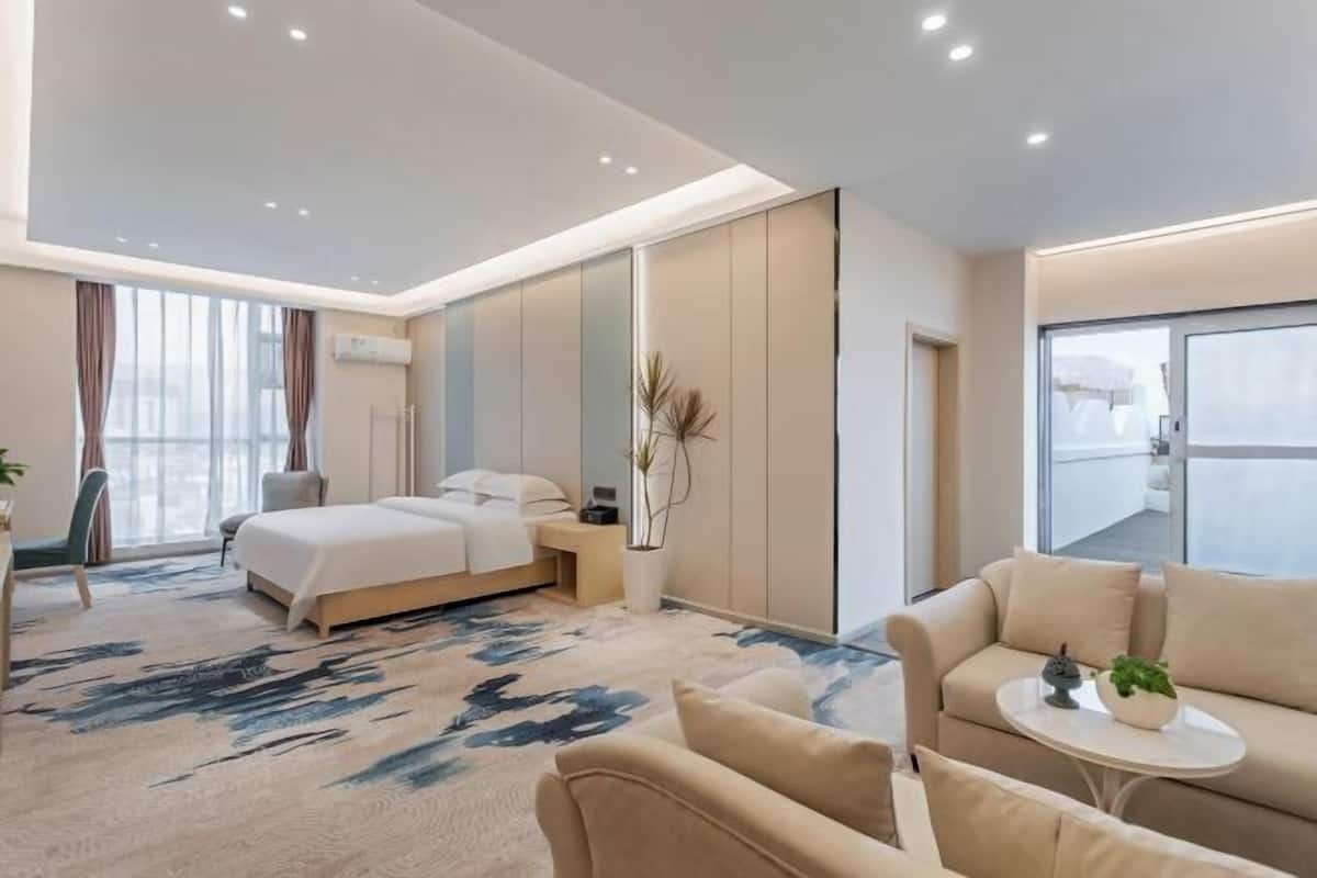A modern hotel room with a bed, sofa, and a small table with a plant.