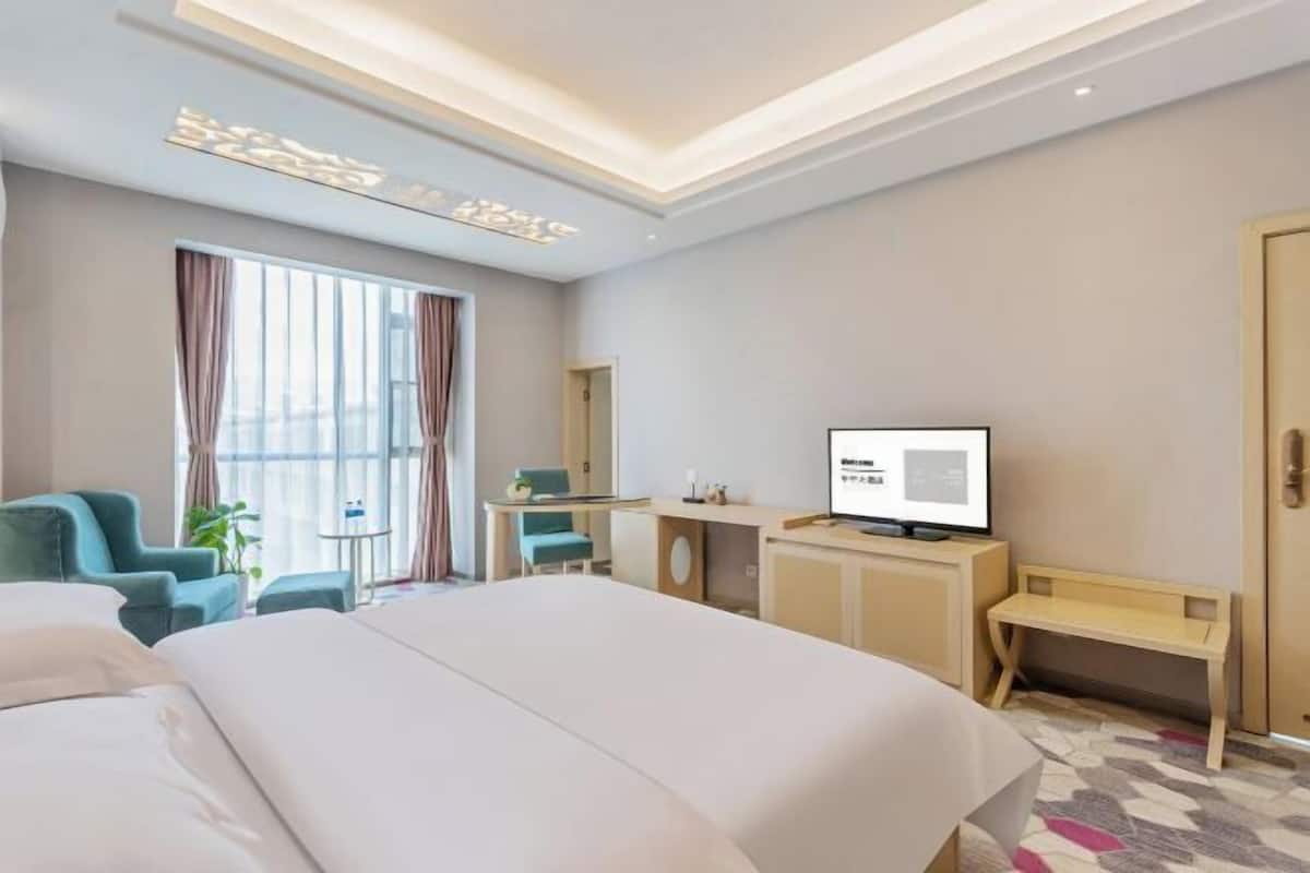 A hotel room with a bed, a desk, a television, and a window with curtains.