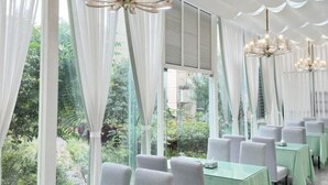 A restaurant with a view of greenery through large windows, white curtains, and multiple chandeliers. - Huaning Hotel (Huaning)