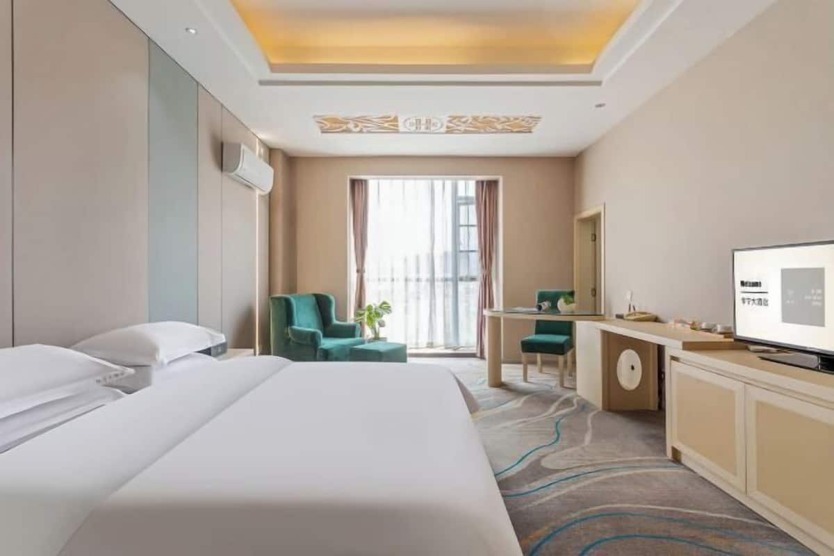 A hotel room with a bed, a desk, a chair, a television, and a window with curtains.