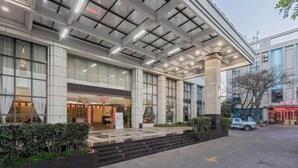 A modern hotel entrance with a glass facade, a covered outdoor seating area, and a parking lot visible in the background. - Huaning Hotel (Huaning)