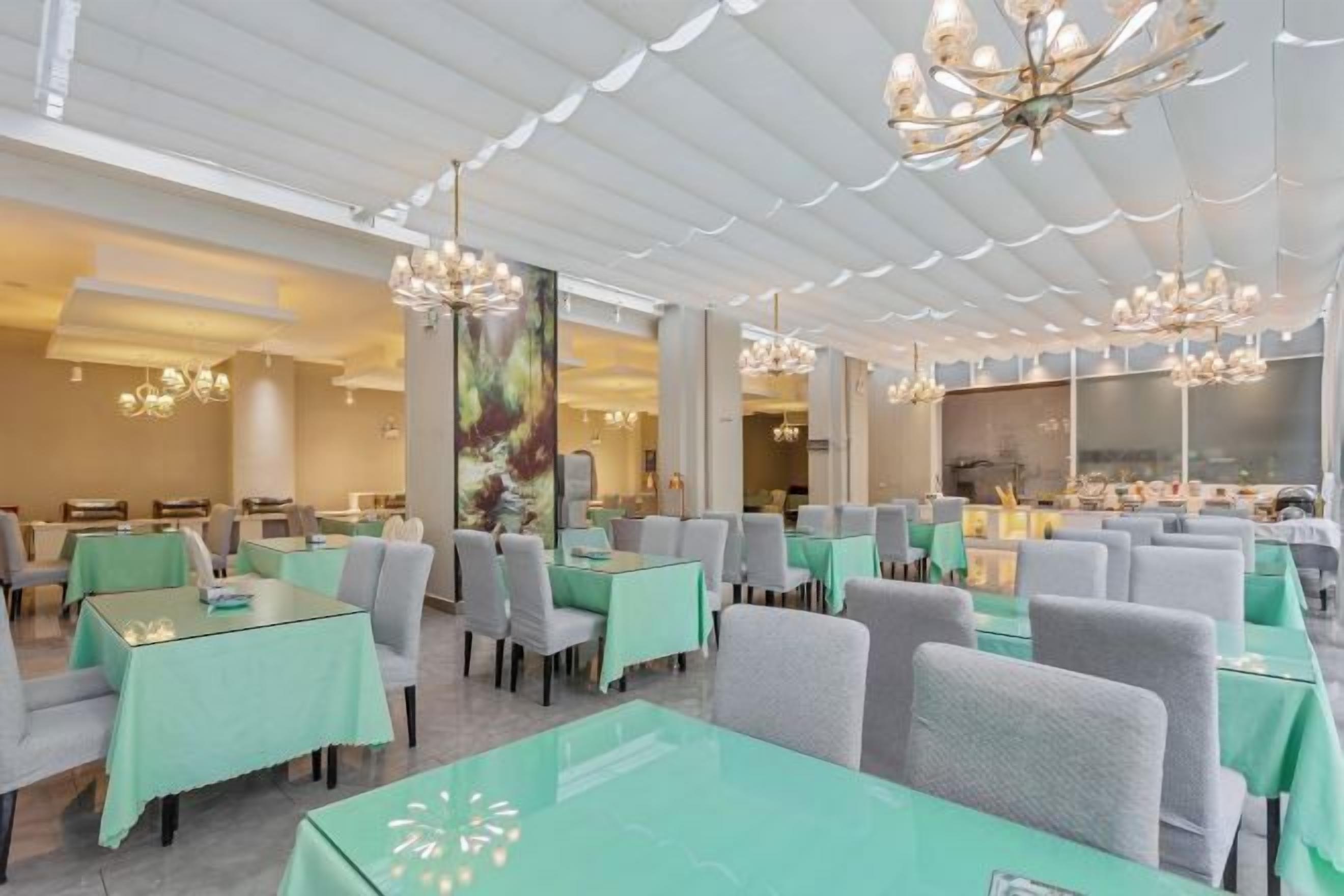 A spacious dining area with multiple tables and chairs, large windows, and decorative lighting fixtures.