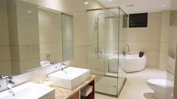 A modern bathroom with a glass-enclosed shower, a large bathtub, and two sinks.