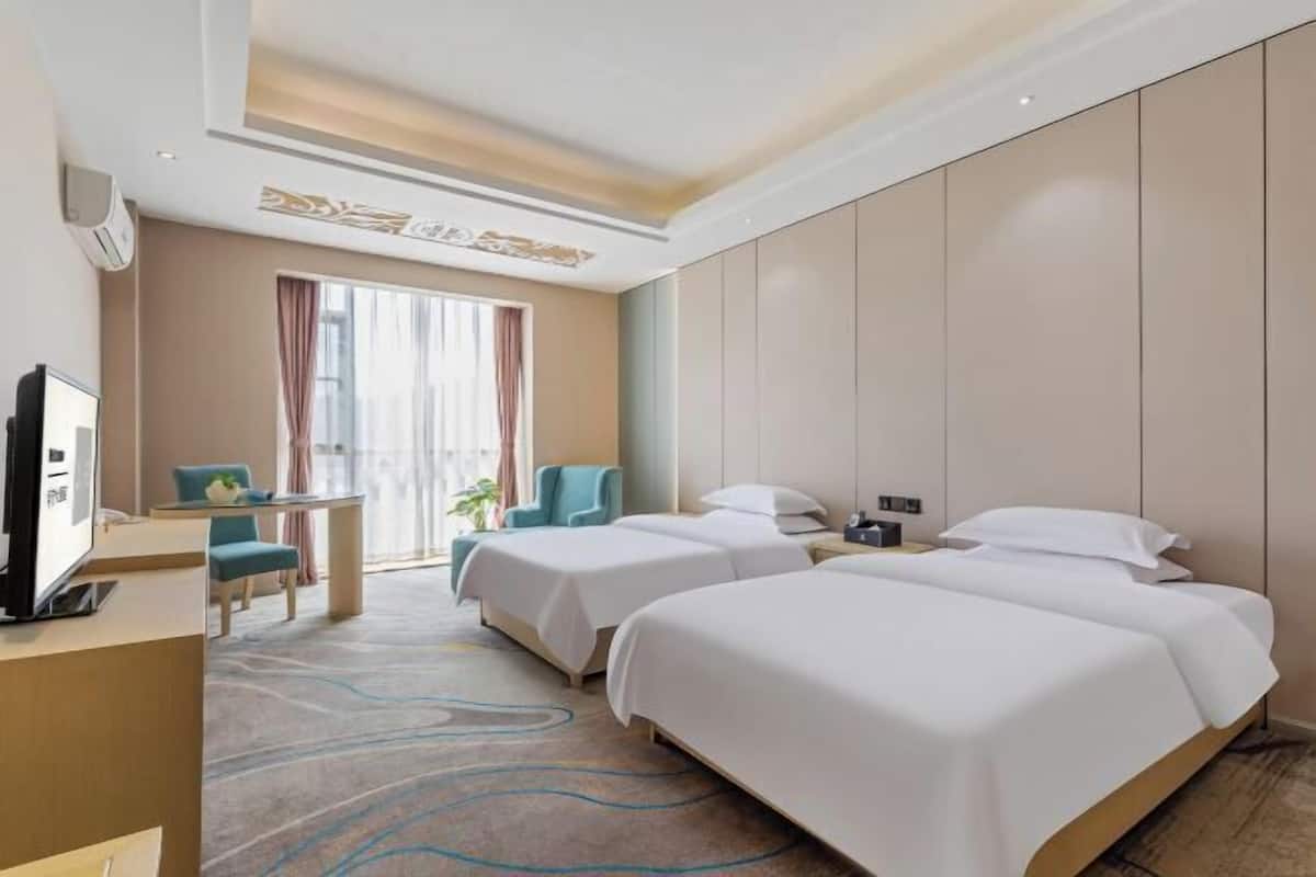 A hotel room with two beds, a desk with a TV, a chair, and a window with curtains.