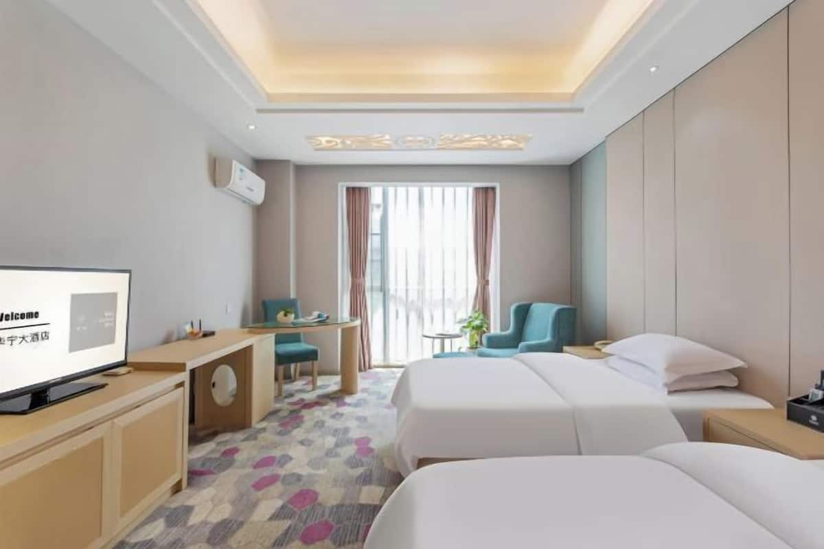 A hotel room with a bed, a desk, a chair, a TV, and a window with curtains.