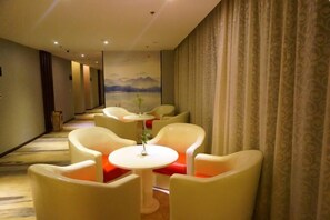 Habitación de hotel con un largo pasillo, sillones blancos, mesitas redondas y un mural en la pared.
