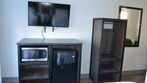 A compact kitchenette with a microwave, refrigerator, and a flat-screen TV mounted on the wall. - Noble Suites Jacksonville (Jacksonville)