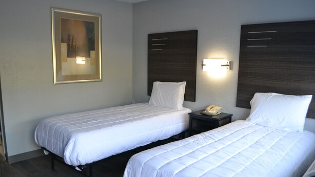 A hotel room with two single beds, a bedside table with a phone, and a wall-mounted light fixture. - Noble Suites Jacksonville (Jacksonville)
