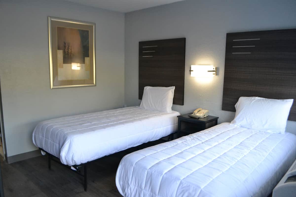 A hotel room with two single beds, a bedside table with a phone, and a wall-mounted light fixture.