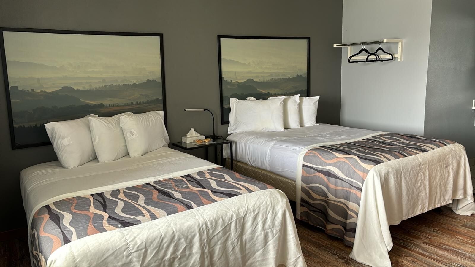 Ett hotellrum med två sängar, var och en med ett mönstrat överkast och vita sängkläder. På väggen ovanför sängarna hänger två inramade landskapsmålningar.