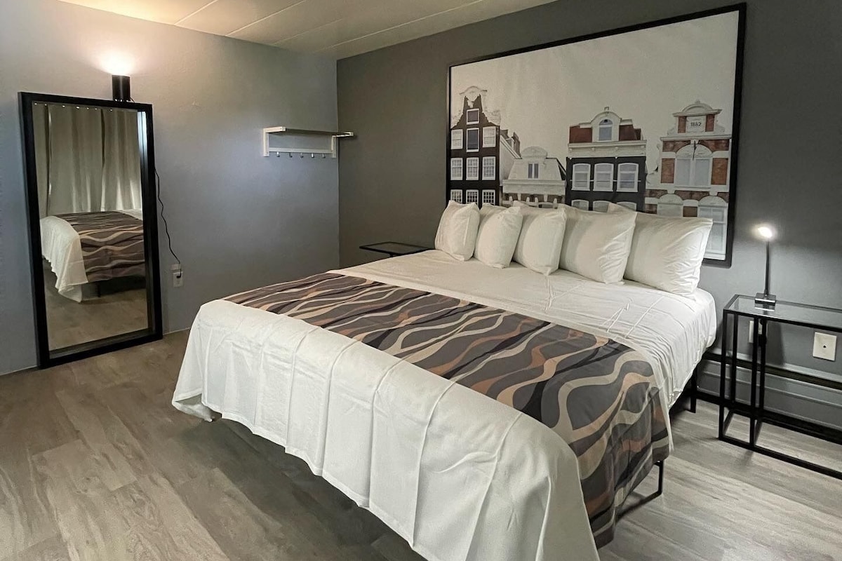 A modern bedroom with a large bed, a mirror, a nightstand, and a painting on the wall.