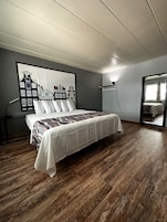 Un dormitorio con cama, un cuadro grande enmarcado en la pared y suelo de madera.