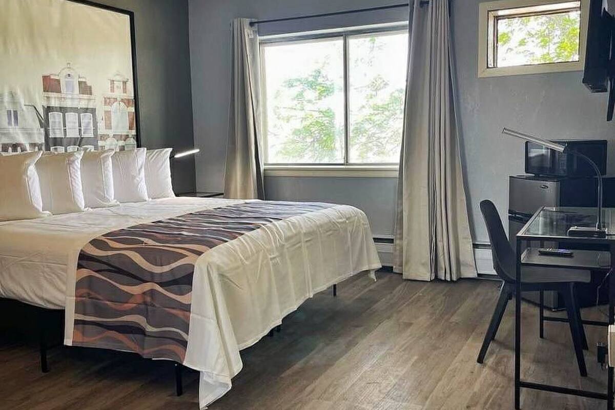 Habitación de hotel con cama, escritorio con ordenador y ventana con cortinas.