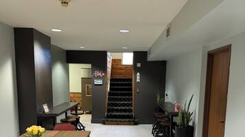 A modern hotel lobby with a wooden reception desk, a staircase, and potted plants.