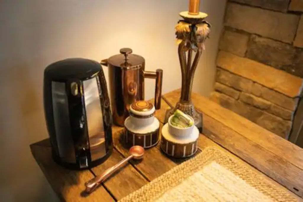 Ein Holztisch mit einer Kaffeemaschine, einem Wasserkocher, einem Teekessel und einer Zuckerdose.