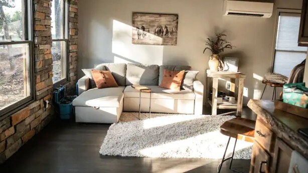 A cozy living room with a sectional sofa, a small table, and a rug. There are large windows on one side and a brick wall on the other. - Little Bit Farm - Create your own stay (Canton)